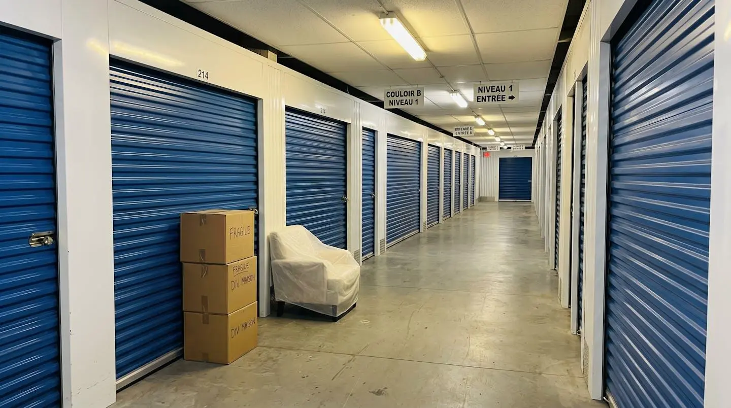 Trois box de stockage de tailles différentes vus en perspective, avec cartons empilés et quelques meubles protégés par des housses